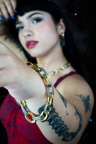 Woman wearing gold and silver chain bracelets with a dark background