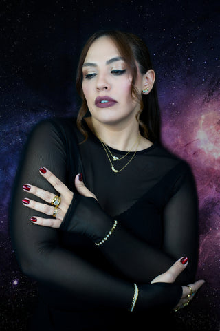 Woman in a black outfit with gold plated jewelry against a starry space background