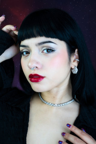 Woman with dark hair and red lipstick wearing a diamond necklace, earrings and ear-cuff against a dark background