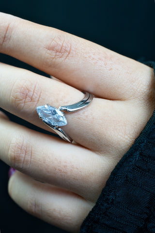 Close-up of a hand wearing a silver ring with a clear gemstone.