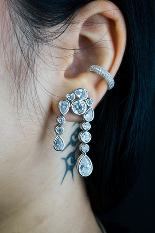 Close-up of an ear wearing a silver dangle silver earring with teardrop-shaped stones