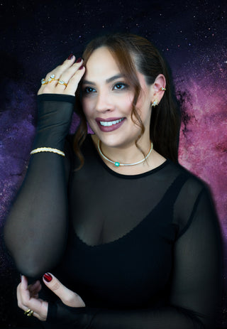 woman wearing gold choker necklace with zirconias and a green gemstone in the middle with white background