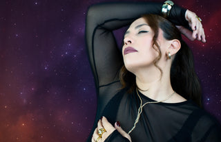 Woman in a black outfit with gold trendy jewelry against a starry space background